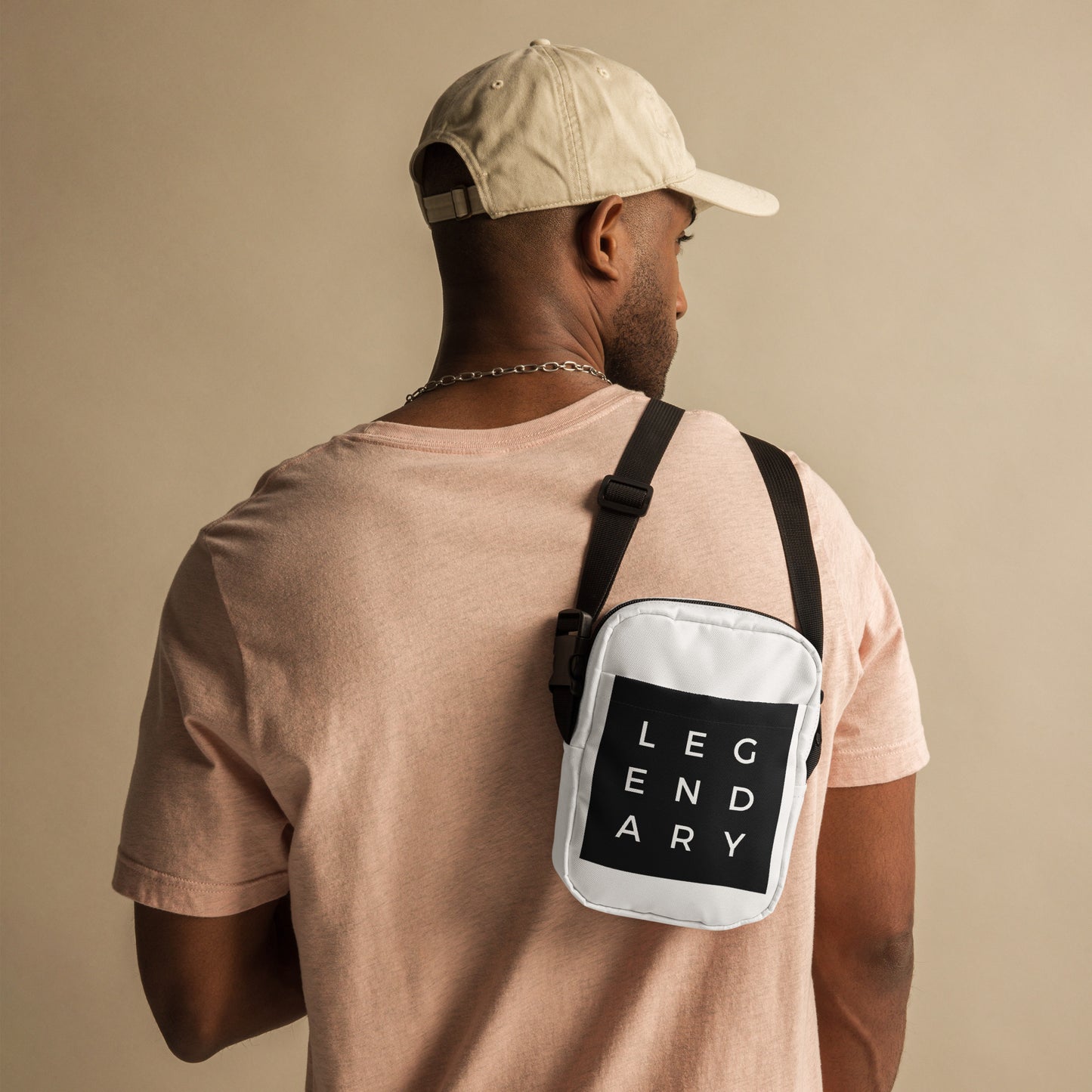 
                  
                    White crossbody bag with black strap and front logo patch, worn on back
                  
                
