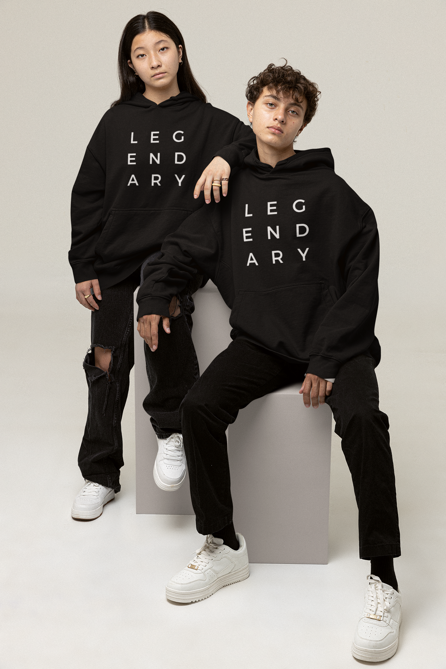 
                  
                    Unisex black hoodie with hood and 'LEGENDARY' lettering, worn by two models
                  
                